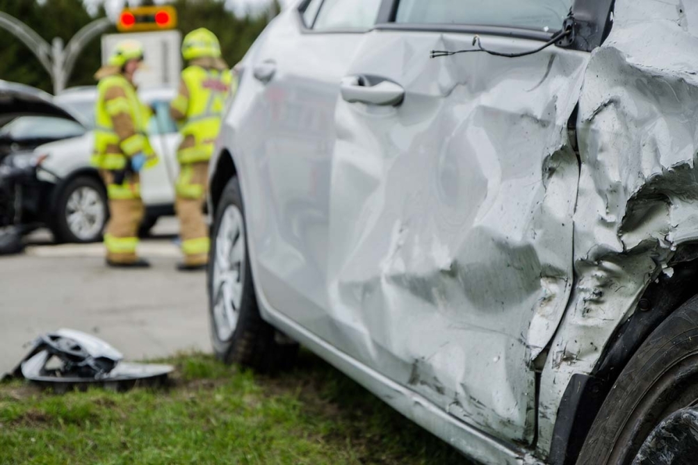 Severely damaged vehicles at the scene of a fatal car crash, with emergency response activity visible on the roadway.