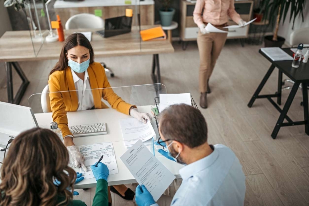 Couple signing a document on a meeting at insurance agent office wearing protective gloves and face mask