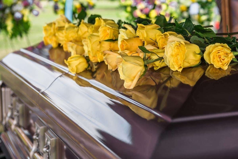 Wooden casket at a funeral service, surrounded by flowers in a solemn indoor setting